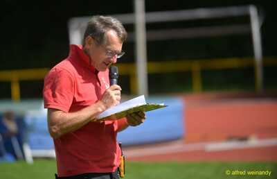 Eine Person liest mit Mikrofon und Klemmbrett Informationen vor, beim Walfried-Heinz-Sportfest der TG Konz im Saar-Mosel-Stadion in Konz.