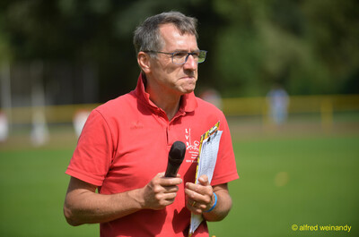 Eine Person spricht mit Mikrofon und Ergebnisliste in der Hand, beim Walfried-Heinz-Sportfest der TG Konz im Saar-Mosel-Stadion in Konz.