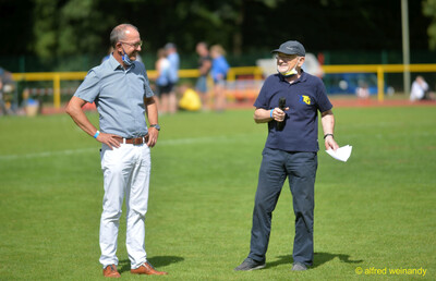 Zwei Verantwortliche unterhalten sich mit Mikrofon auf dem Rasen beim Walfried-Heinz-Sportfest der TG Konz im Saar-Mosel-Stadion in Konz.