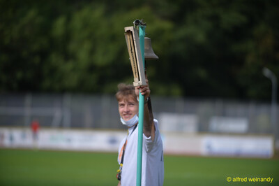 Eine Person hält die Rundenglocke mit Anzeigetafel an einer Stange hoch beim Walfried-Heinz-Sportfest der TG Konz im Saar-Mosel-Stadion in Konz.