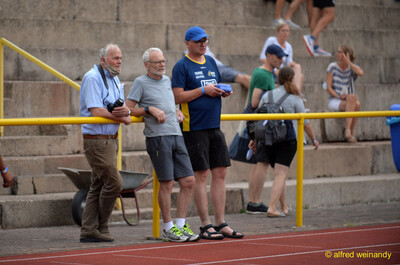 Zuschauende und Betreuende beobachten den Wettkampf am Bahnrand beim Walfried-Heinz-Sportfest der TG Konz im Saar-Mosel-Stadion in Konz.