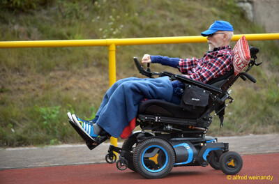 Eine Person sitzt mit Decke in einem Elektrorollstuhl auf der roten Laufbahn beim Walfried-Heinz-Sportfest der TG Konz im Saar-Mosel-Stadion in Konz.