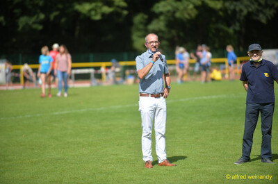 Eine Person mit Mikrofon steht auf dem Rasen beim Walfried-Heinz-Sportfest der TG Konz im Saar-Mosel-Stadion in Konz.