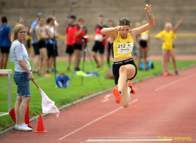 Eine junge Person schwebt in der Flugphase des Dreisprungs über der Anlaufbahn, beim Walfried-Heinz-Sportfest der TG Konz im Saar-Mosel-Stadion in Konz.