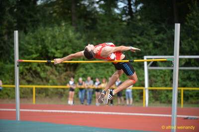 Eine Person im roten Trikot überquert in Fosbury-Flop-Technik die Latte beim Walfried-Heinz-Sportfest der TG Konz im Saar-Mosel-Stadion in Konz.