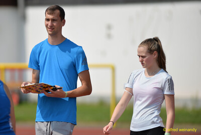 Eine Person im Helferdienst mit Klemmbrett und eine junge Person stehen am Rand der Laufbahn beim Walfried-Heinz-Sportfest der TG Konz im Saar-Mosel-Stadion in Konz.