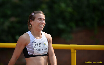 Eine Person mit Startnummer lächelt nach einem Wettkampf am Rand der Laufbahn beim Walfried-Heinz-Sportfest der TG Konz im Saar-Mosel-Stadion in Konz.