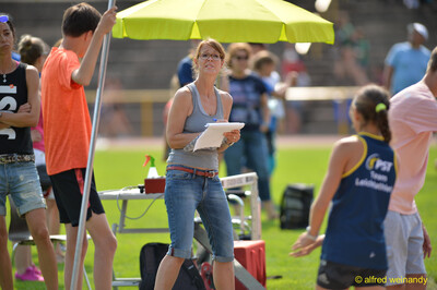 Eine Person im Kampfgericht notiert mit Klemmbrett die Ergebnisse unter einem Sonnenschirm beim Walfried-Heinz-Sportfest der TG Konz im Saar-Mosel-Stadion in Konz.