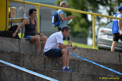 Personen im Helferdienst und die Stadionmoderation sitzen auf den Tribünenstufen beim Walfried-Heinz-Sportfest der TG Konz im Saar-Mosel-Stadion in Konz.