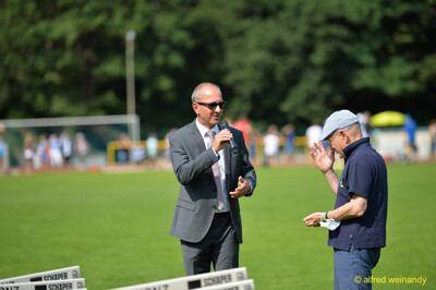 Zwei Personen unterhalten sich mit Mikrofon auf dem Sportplatz beim Walfried-Heinz-Sportfest der TG Konz im Saar-Mosel-Stadion in Konz.