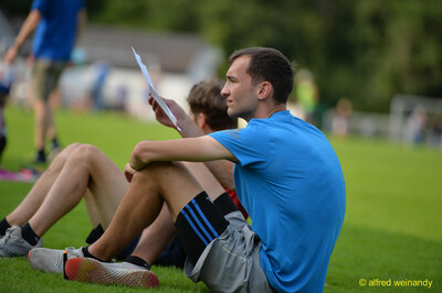 Eine junge Person sitzt im Gras und liest ihre Ergebnisliste beim Walfried-Heinz-Sportfest der TG Konz im Saar-Mosel-Stadion in Konz.