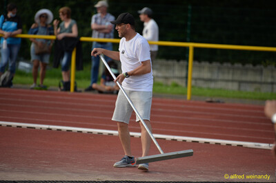 Eine Person zieht mit einem Abzieher das Wasser von der Laufbahn beim Walfried-Heinz-Sportfest der TG Konz im Saar-Mosel-Stadion in Konz.