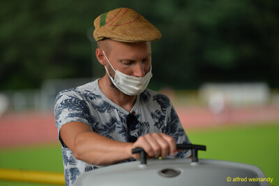 Eine Person mit Mundschutz und Schirmmütze richtet am Rand der Bahn ein Sportgerät her beim Walfried-Heinz-Sportfest der TG Konz im Saar-Mosel-Stadion in Konz.