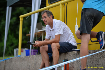 Eine Person aus der Moderation sitzt mit Mikrofon am Rand der Anlage beim Walfried-Heinz-Sportfest der TG Konz im Saar-Mosel-Stadion in Konz.