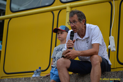 Eine Person aus der Moderation spricht mit Mikrofon neben einem Kind beim Walfried-Heinz-Sportfest der TG Konz im Saar-Mosel-Stadion in Konz.