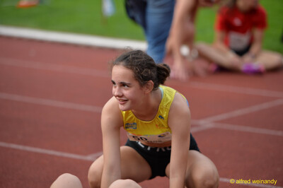 Eine jugendliche Person hockt lächelnd auf der Laufbahn und macht eine Pause beim Walfried-Heinz-Sportfest der TG Konz im Saar-Mosel-Stadion in Konz.