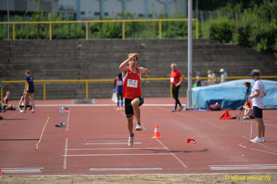 Eine Person streckt sich in der Flugphase über der Dreisprunganlage mit der Sandgrube im Vordergrund beim Walfried-Heinz-Sportfest der TG Konz im Saar-Mosel-Stadion in Konz.
