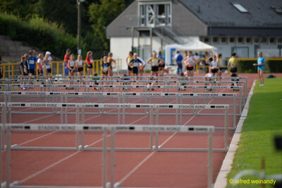 Aufgebaute Hürden stehen für den Hürdenlauf bereit, während junge Aktive im Hintergrund warten, beim Walfried-Heinz-Sportfest der TG Konz im Saar-Mosel-Stadion in Konz.