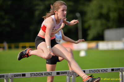 Eine junge Person springt im Hürdenlauf über eine Hürde beim Walfried-Heinz-Sportfest der TG Konz im Saar-Mosel-Stadion in Konz.