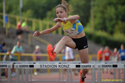 Eine junge Person springt im Hürdenlauf über eine Hürde beim Walfried-Heinz-Sportfest der TG Konz im Saar-Mosel-Stadion in Konz.
