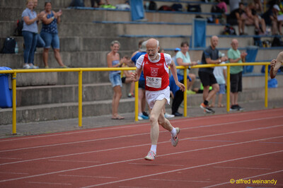 Eine ältere Person im rot-weißen Trikot mit der Startnummer 265 sprintet über die Rundbahn beim Walfried-Heinz-Sportfest der TG Konz im Saar-Mosel-Stadion in Konz.