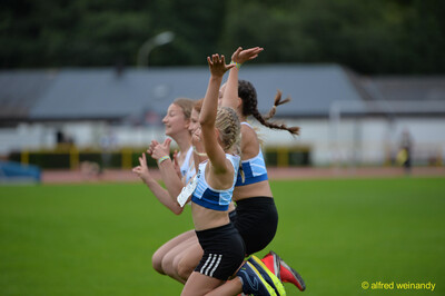 Jugendliche reißen im Zieleinlauf eines Laufs jubelnd die Arme hoch beim Walfried-Heinz-Sportfest der TG Konz im Saar-Mosel-Stadion in Konz.