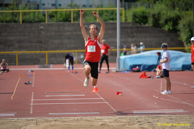 Eine Person im Weitsprung in der Flugphase mit nach oben gestreckten Armen über der Sandgrube beim Walfried-Heinz-Sportfest der TG Konz im Saar-Mosel-Stadion in Konz.