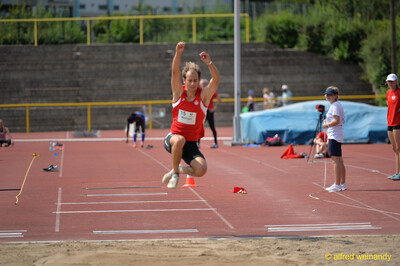 Eine Person zieht beim Weitsprung in der Flugphase die Knie an, kurz vor der Landung in der Sandgrube beim Walfried-Heinz-Sportfest der TG Konz im Saar-Mosel-Stadion in Konz.
