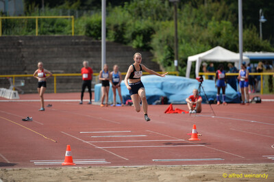 Eine junge Person in der Flugphase beim Weitsprung über der Anlaufbahn vor der Sandgrube beim Walfried-Heinz-Sportfest der TG Konz im Saar-Mosel-Stadion in Konz.