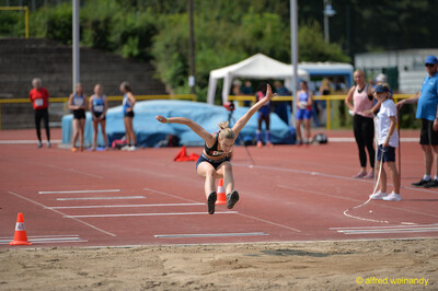 Eine Person schwebt beim Weitsprung mit ausgebreiteten Armen in der Flugphase über der Sandgrube beim Walfried-Heinz-Sportfest der TG Konz im Saar-Mosel-Stadion in Konz.