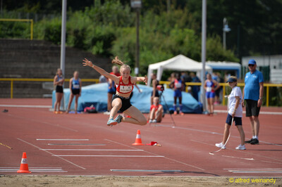 Eine junge Person in der Flugphase beim Weitsprung mit ausgebreiteten Armen über der Sandgrube beim Walfried-Heinz-Sportfest der TG Konz im Saar-Mosel-Stadion in Konz.