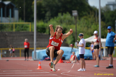 Eine Person in der Flugphase des Weitsprungs mit angezogenen Knien beim Walfried-Heinz-Sportfest der TG Konz im Saar-Mosel-Stadion in Konz.