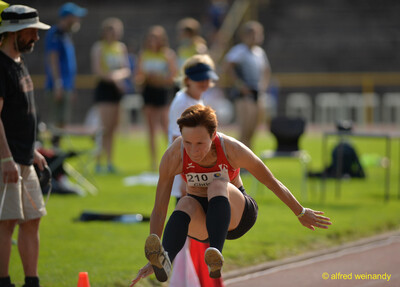 Eine Person im roten Top fliegt mit angehockten Beinen zur Landung beim Weitsprung beim Walfried-Heinz-Sportfest der TG Konz im Saar-Mosel-Stadion in Konz.