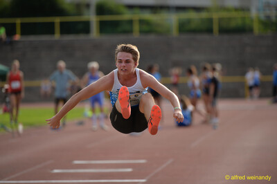Eine junge Person fliegt im Weitsprung mit gestreckten Beinen durch die Luft beim Walfried-Heinz-Sportfest der TG Konz im Saar-Mosel-Stadion in Konz.
