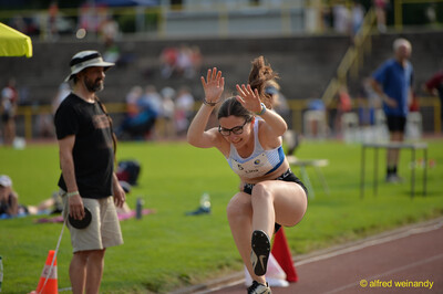 Eine Person mit Sportbrille und Startnummer 5 landet nach einem Sprung neben der Anlaufbahn beim Walfried-Heinz-Sportfest der TG Konz im Saar-Mosel-Stadion in Konz.
