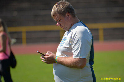 Eine Person schaut am Rand des Sportplatzes auf ihr Handy bei der Rheinland-Meisterschaft im Mehrkampf der TG Konz in Konz.