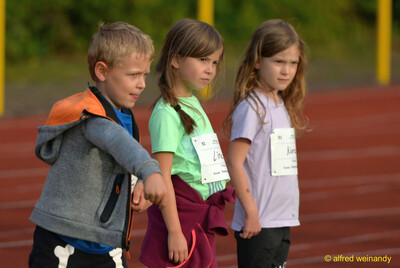 Drei Kinder mit Startnummern gehen nebeneinander über die Laufbahn beim Jugendsportfest der TG Konz in Konz