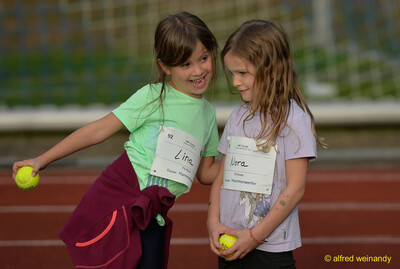 Zwei Kinder lachen gemeinsam und halten kleine Bälle in den Händen an der Laufbahn beim Jugendsportfest der TG Konz in Konz.