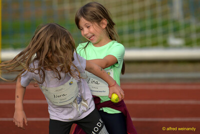 Zwei Kinder albern ausgelassen miteinander auf der Laufbahn, eines hält einen kleinen Ball, beim Jugendsportfest der TG Konz in Konz.