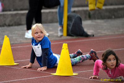 Zwei Kinder absolvieren am Boden liegend eine Übung an gelben Pylonen auf der Laufbahn beim Jugendsportfest der TG Konz in Konz.