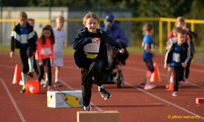Ein Kind läuft und springt auf einem Parcours über aufgestellte Kartons auf der Laufbahn beim Jugendsportfest der TG Konz in Konz.