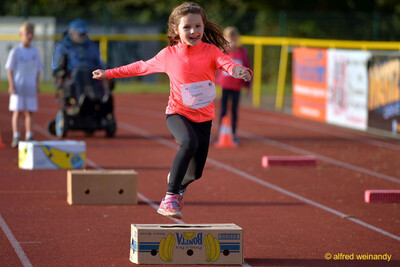 Ein Kind springt schwungvoll über einen Karton auf dem Hindernisparcours beim Jugendsportfest der TG Konz in Konz.