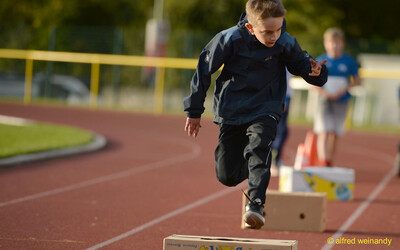 Ein Kind springt konzentriert über einen Karton des Hindernisparcours auf der Laufbahn beim Jugendsportfest der TG Konz in Konz.