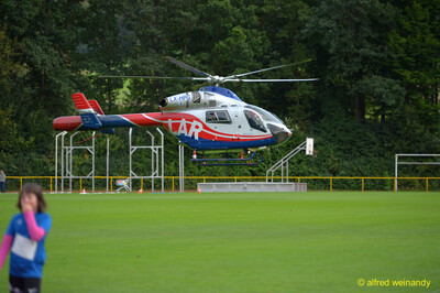 Ein rot-weißer Rettungshubschrauber schwebt über dem Rasenplatz, im Vordergrund ein Kind, beim Jugendsportfest der TG Konz in Konz