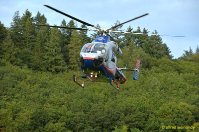 Ein Rettungshubschrauber fliegt vor einem bewaldeten Hang beim Jugendsportfest der TG Konz in Konz.