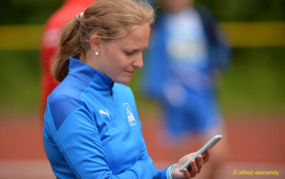 Eine Person in blauer Vereinsjacke blickt konzentriert auf ihr Smartphone am Rand der Wettkampfstätte, bei der Rheinland-Pfalz-Meisterschaft in Konz.