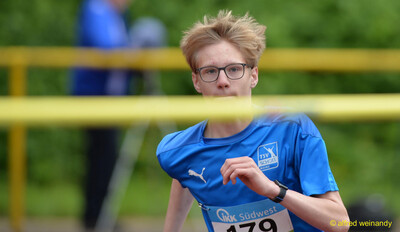 Nahaufnahme einer jungen Person im blauen Trikot in Laufbewegung hinter einer gelben Absperrung, bei der Rheinland-Pfalz-Meisterschaft in Konz.