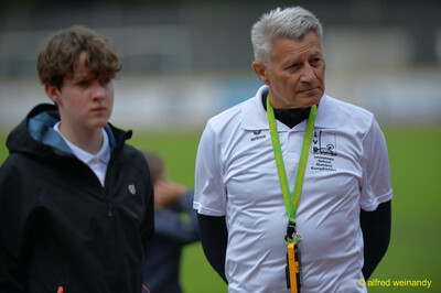 Eine Person im Kampfgericht und eine Person im Helferdienst stehen auf dem Sportplatz bei der Rheinland-Pfalz-Meisterschaft in Konz.