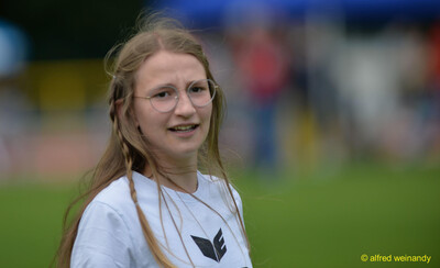 Eine Person mit Brille lächelt in die Kamera am Rand des Sportplatzes bei der Rheinland-Pfalz-Meisterschaft in Konz.