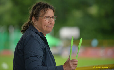 Eine Person hält grüne Grillzangen in der Hand und lächelt am Rand der Sportanlage bei der Rheinland-Pfalz-Meisterschaft in Konz.